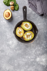 Quail eggs baked in avocado. Avocado egg boats in cast-iron pan on gray background.  Top view. Copy space.