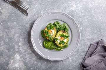 Quail eggs baked in avocado. Avocado egg boats served with spinach leaves on gray plate . Ketogenic, keto low carb diet. Food background. Top view. Copy space.