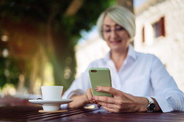 Mature woman using mobile phone while sitting at a cafe and drinking coffee 