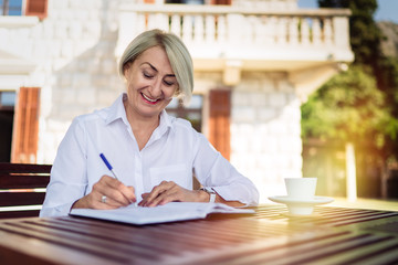 Happy senior woman writing to notebook or diary at a cafe