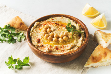 Hummus dip with chickpea, pita  and parsley in wooden plate on white background