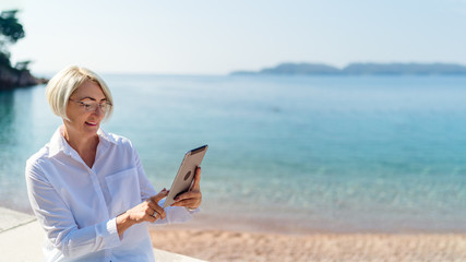 Mature woman using tablet on background the sea and blue sky