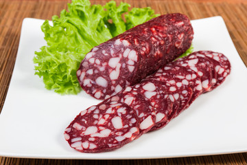 Partly sliced dry-cured sausage on dish close-up