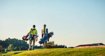 Poster Happy couple carrying stand bags towards the golf course in a sunny day © Kzenon