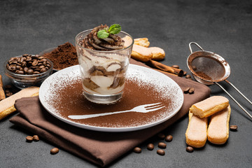 Classic tiramisu dessert in a glass and cup of coffee on dark concrete background