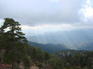 An unusual natural picture of the rays of the sun that penetrates through a heavy gray cloud to dense forests on the slopes of the mountains.