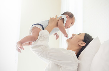 Portrait of mother lifting and playing with newborn baby, baby talking to mother. Health care...