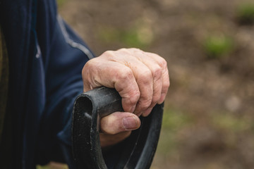 an old man's hand holds a shovel handle