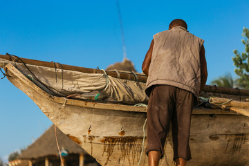 Poor African fisherman repairing his old wooden boat on the ocean