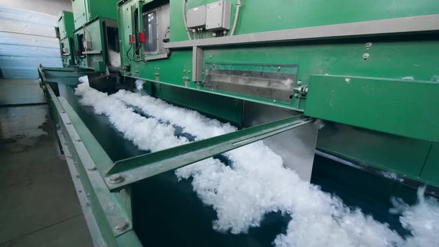 Factory machines work with white polyester fiber, moving it onto a conveyor.