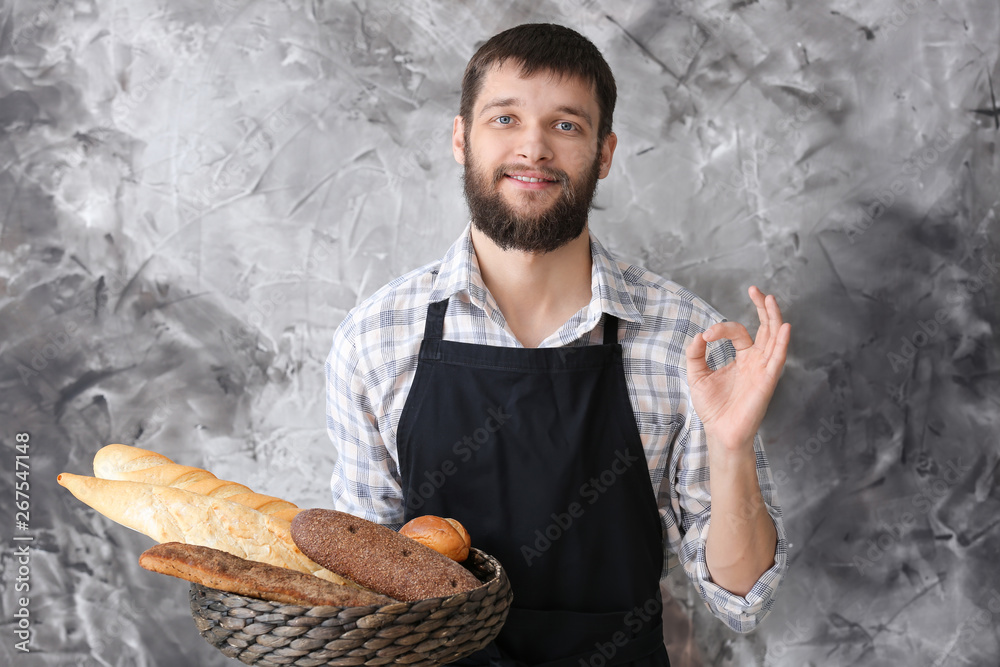 Poster Young baker with fresh bread showing OK gesture on color background