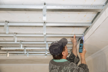 Man is working with a drill and making stretch ceiling. Maintenance repair works renovation in the flat. Restoration indoors.