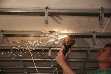 Man is working with an angle grinder and making stretch ceiling. Maintenance repair works renovation in the flat. Restoration indoors. Sparks.