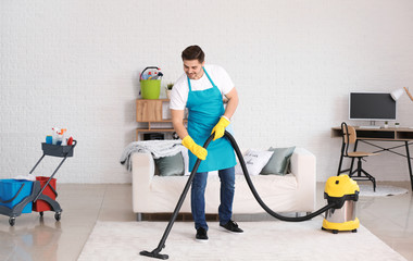 Male janitor hoovering carpet in flat