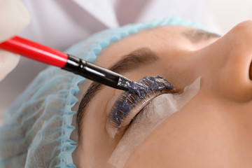 Young woman undergoing procedure of eyelashes dyeing and lamination in beauty salon, closeup