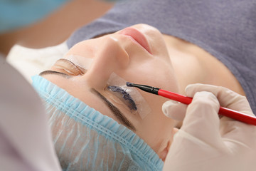 Young woman undergoing procedure of eyelashes dyeing and lamination in beauty salon