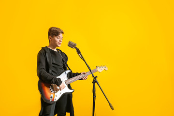 Teenage boy with microphone singing and playing guitar against color background