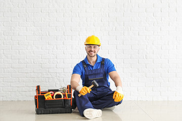 Male electrician with tools kit sitting near white brick wall