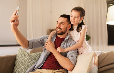 people, family and technology concept - happy father and little daughter taking selfie by smartphone at home