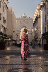 Naklejka premium Young blonde tourist woman walking on the Rua Augusta street in Lisbon city and exploring old architecture, Portugal