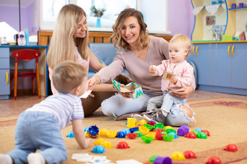 Naklejka na ściany i meble Nursery babies playing with toys. Mothers communicate and look after their children