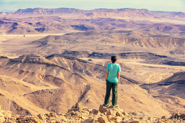 Fototapeta premium A man stands on the edge of a cliff in the desert and looks at a beautiful view.