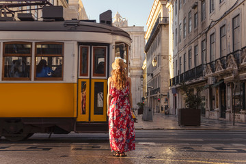 Young blonde tourist woman looking at passing typical Lisbon yellow tram on the street in the city centre on Rua Augusta