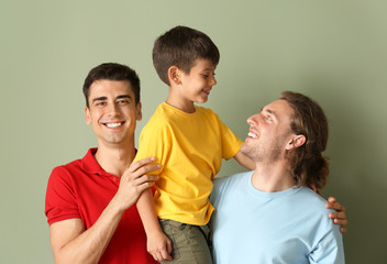 Happy gay couple with adopted child on color background