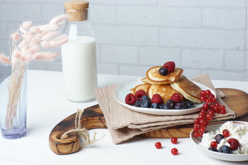 Breakfast on a white table, pancakes with berries, fresh cottage cheese and a bottle of milk
