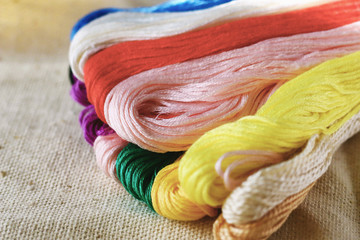 multi-colored colorful rainbow colors threads for embroidery floss on light fabric canvas close-up,...