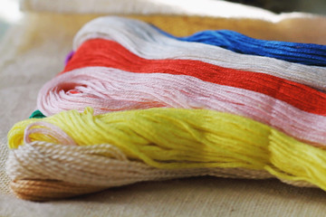 multi-colored colorful rainbow colors threads for embroidery floss on light fabric canvas close-up,...