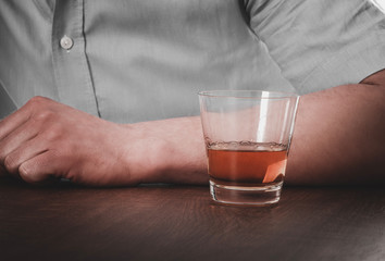 Man's hand on table with glass of wiskey. Alcohol addoction concept.