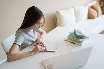 Cute teenager girl sitting at table with books and doing homework. Education, children and school concept     