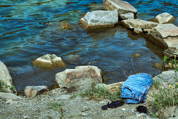 crystal clear blue cool water at the shore of a wild lake in a quarry without people with steep rocky beaches and large boulders on a summer warm day