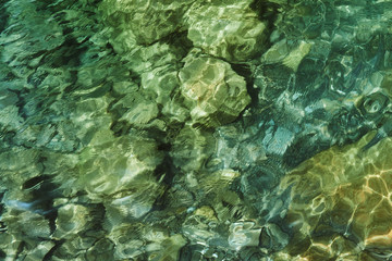 crystal clear blue cool water at the shore of a wild lake in a quarry without people with steep rocky beaches and large boulders on a summer warm day