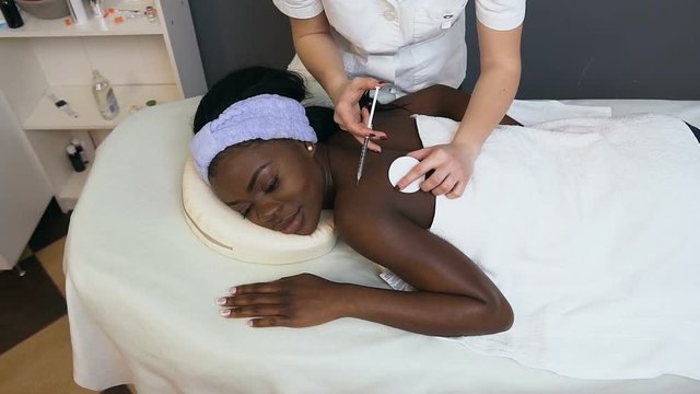 Young cosmetologist making beauty injection for young african woman.