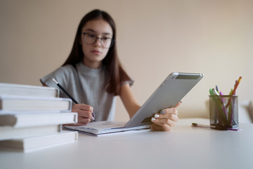 Cute teenager girl sitting at table with books and doing homework. Education, children and school concept      