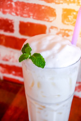 Iced milk with milk foam in tall glass on the wooden table and brick wall in cafe
