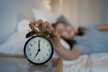 Close up sleepy teenager girl turning alarm off in the morning while lying in bed. Early wake up,...