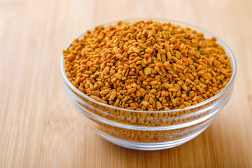 Fenugreek seeds in glass bowl and scoop on wooden background