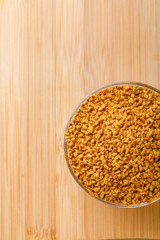 Fenugreek seeds in glass bowl and scoop on wooden background