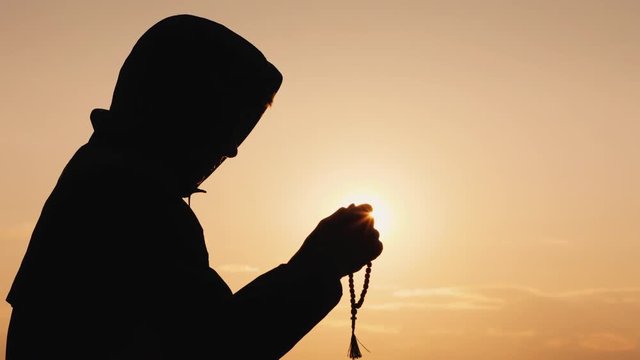 Side view of a man in the hood, sifting through the rosary at sunset