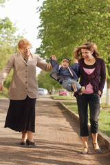 Mom and grandmother are holding hands of the little boy and carry it. Everyone laughs and happy