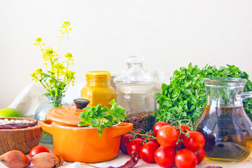 Food and utensils to prepare food. Fresh basil, cherry tomatoes, beans, olive oil, lime, onion, spices, saucepan, jars in cereals. Culinary background. Copy space