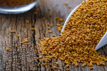 Fenugreek seeds in glass bowl and scoop on wooden background
