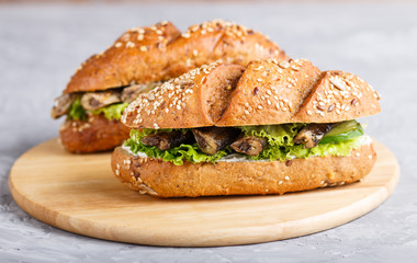 Sprats sandwiches with lettuce and cream cheese on wooden board on a gray concrete background.