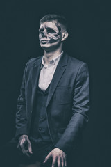 Stylish and beautiful, emotional young man with skeleton makeup in a strict suit against the background of smoke and dark background to Halloween