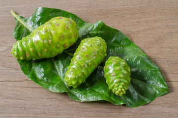 Fruit of Great morinda (Noni) or Morinda citrifolia tree and green leaf on the wood background