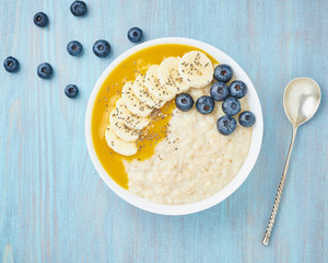 Oatmeal with bananas, blueberries, chia seeds, jam on blue wooden background. Healthy breakfast.