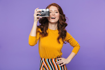 Photo of happy redhead woman wearing yellow clothes holding retro vintage camera and taking picture